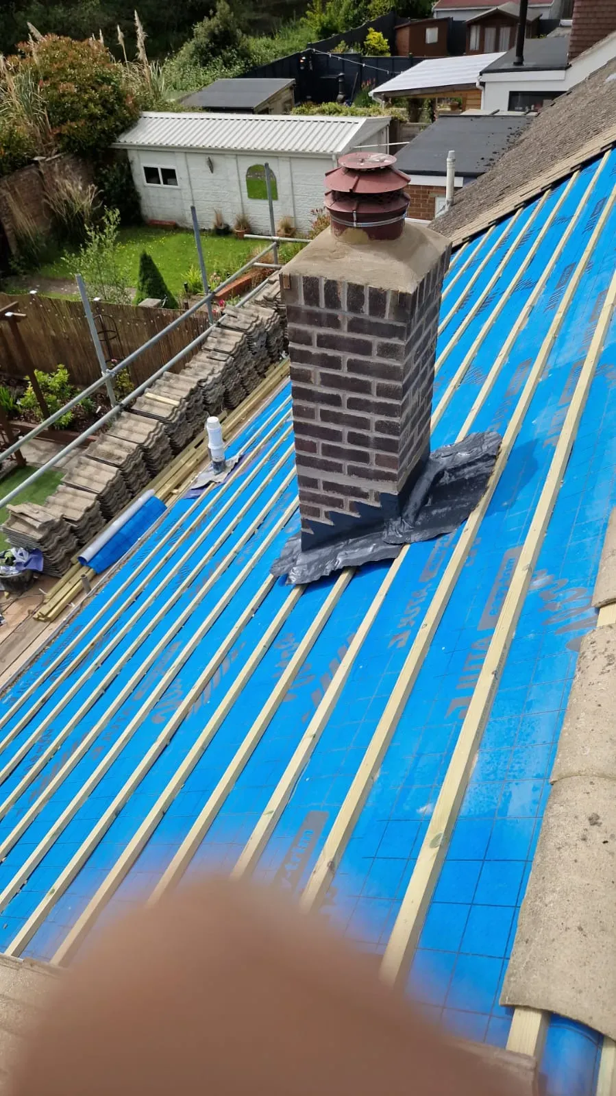 Pitched roof under construction with blue breathable membrane, wooden battens, and a brick chimney with leadwork.