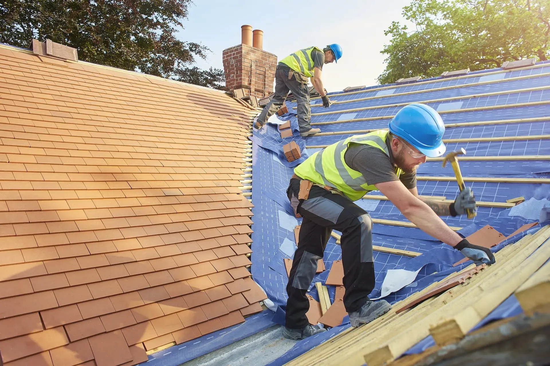 Expert roofers from Trustmark Roofing installing new clay tiles on a pitched roof, demonstrating quality craftsmanship for new roof installations.