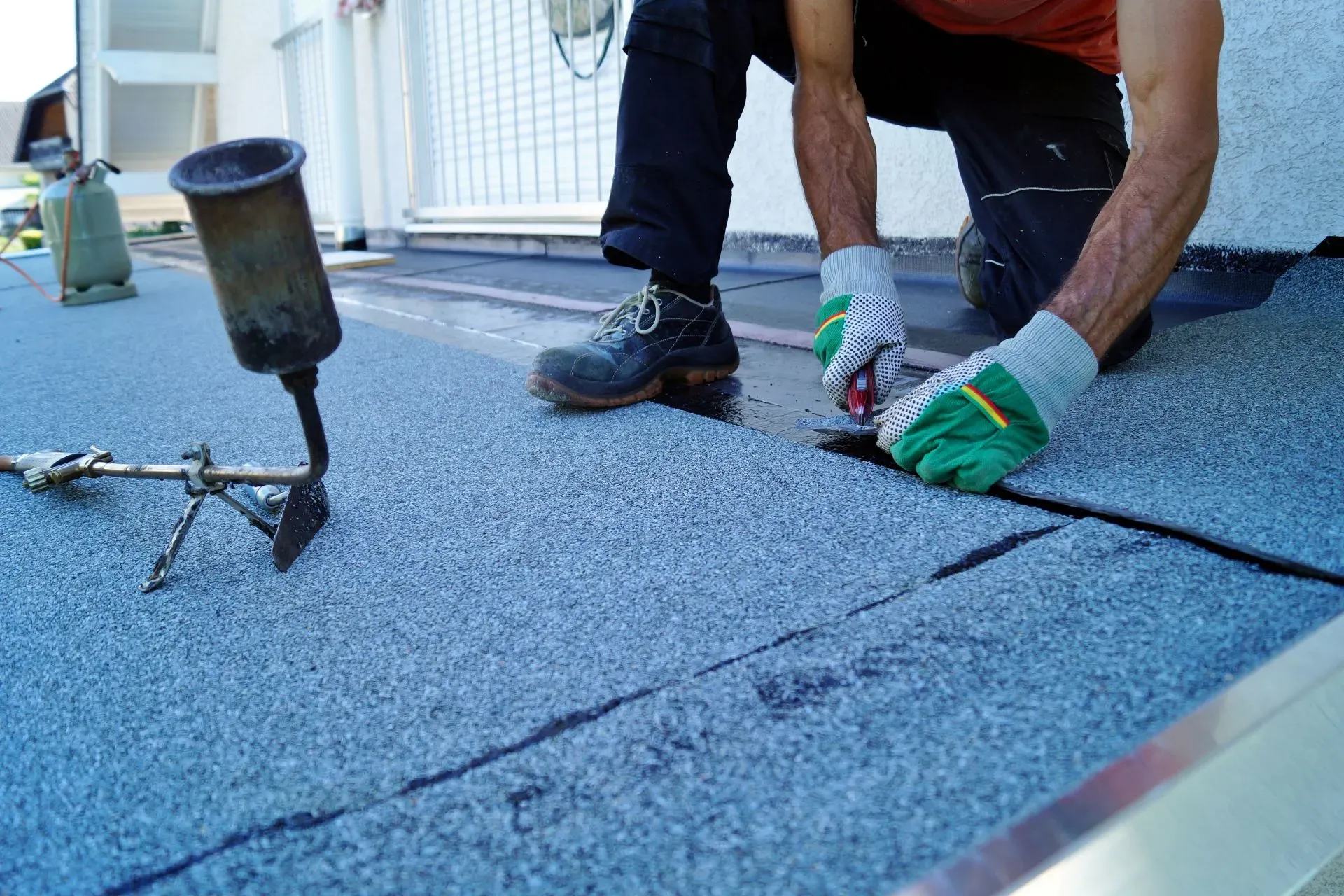 Close-up of a roofer installing a flat roof using a torch-on felt system with granulated membrane, demonstrating professional flat roofing work.