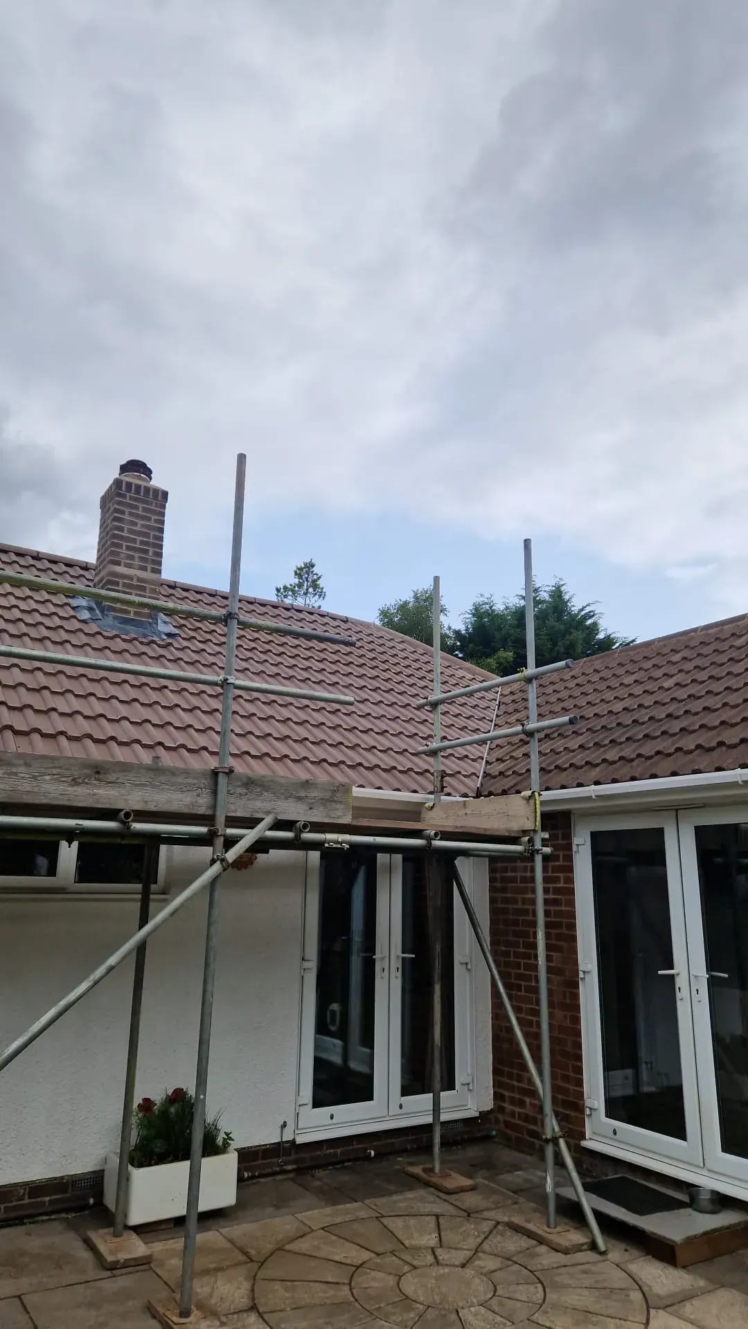 Scaffolding erected in front of a residential house with a brown tiled roof and brick chimney, ready for roofing work or repair.