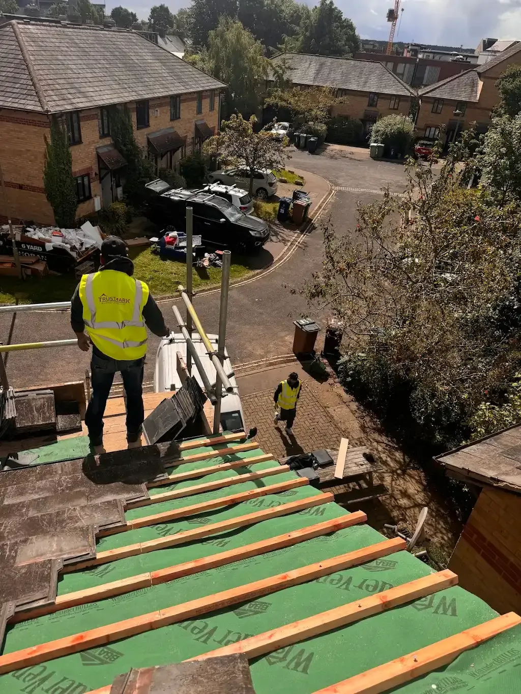 Trustmark Roofing team member installing a new tile roof on a home, featuring green roofing membrane and wooden battens in a residential UK setting.